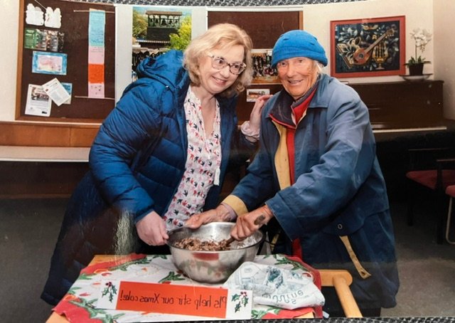 Two people stirring Christmas cake mix together at a community table